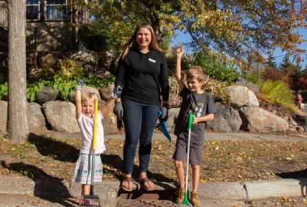 A woman and children rake leaves away from storm drain