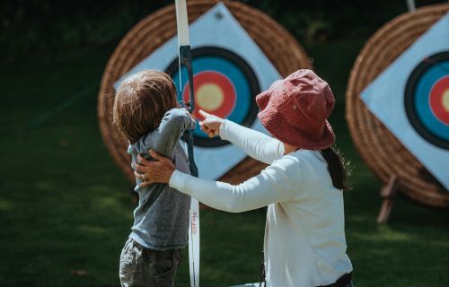 A woman helps a young child practice archery